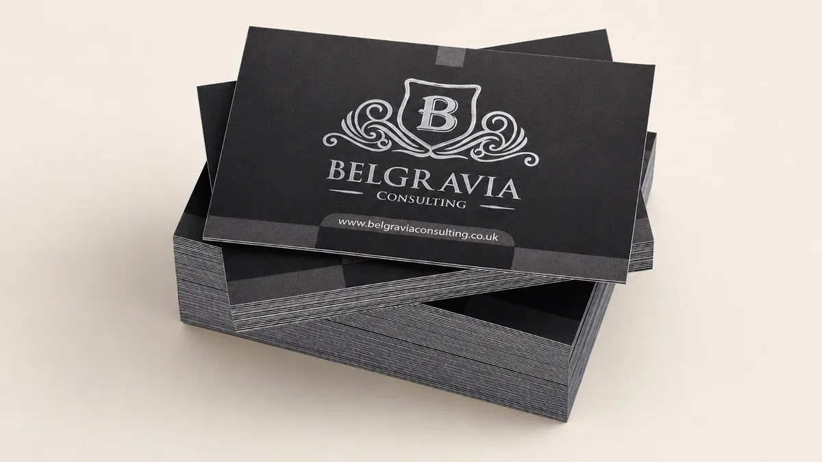 Black premium business cards with silver foil shield monogram, stack edges visible to show Pantone trim finishing